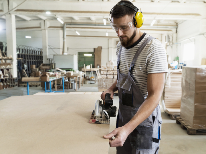 Operador com uma serra elétrica a corta um painel de madeira